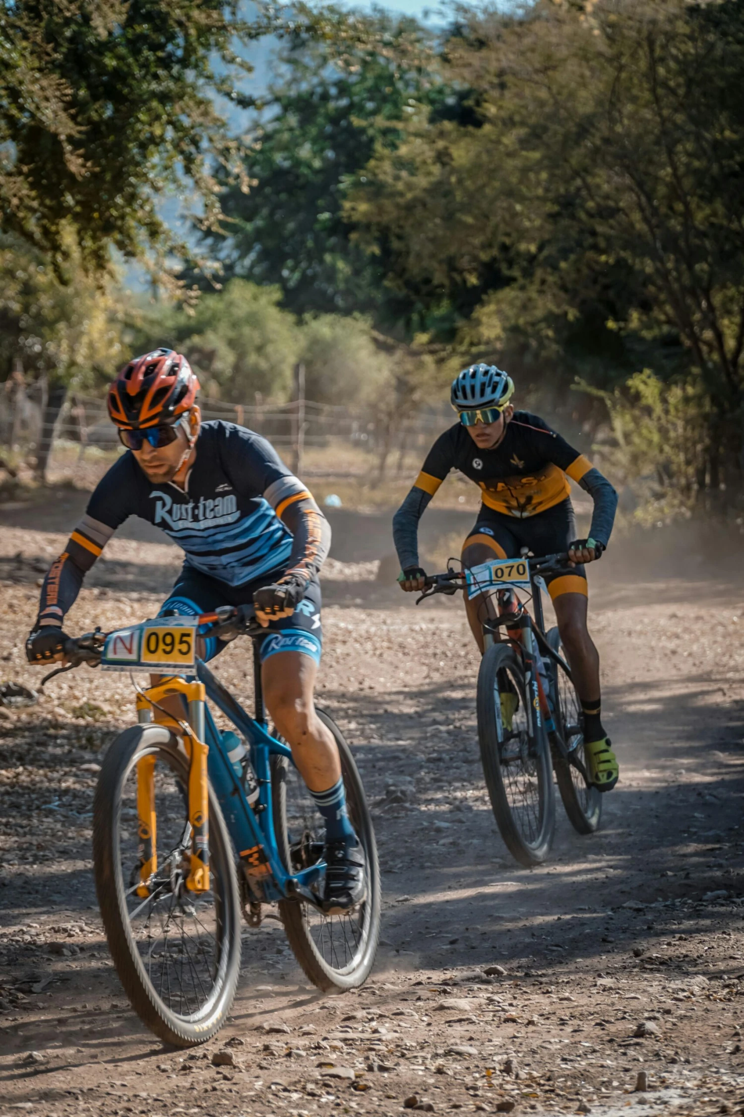 Two cyclists race fiercely on a dusty mountain trail under clear skies.